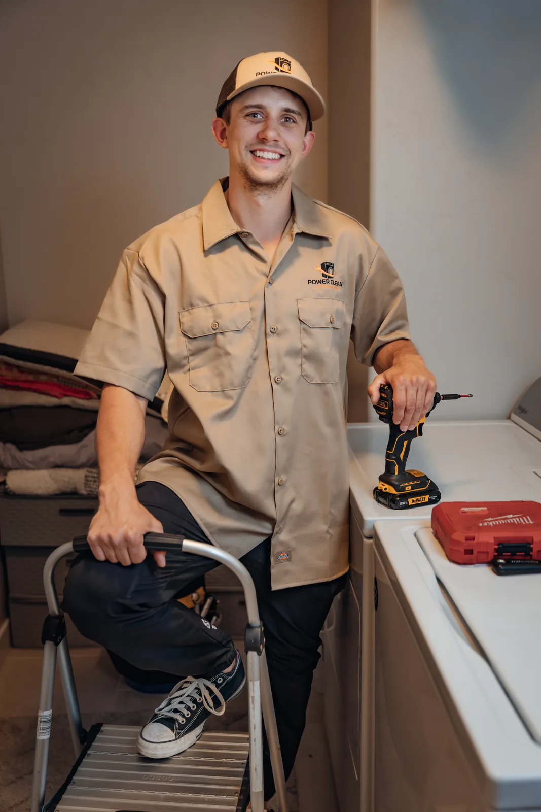 Blake Lonsberry, PowerClean's owner and lead technician, in a laundry room with one foot on a step stool and a hand on his impact driver