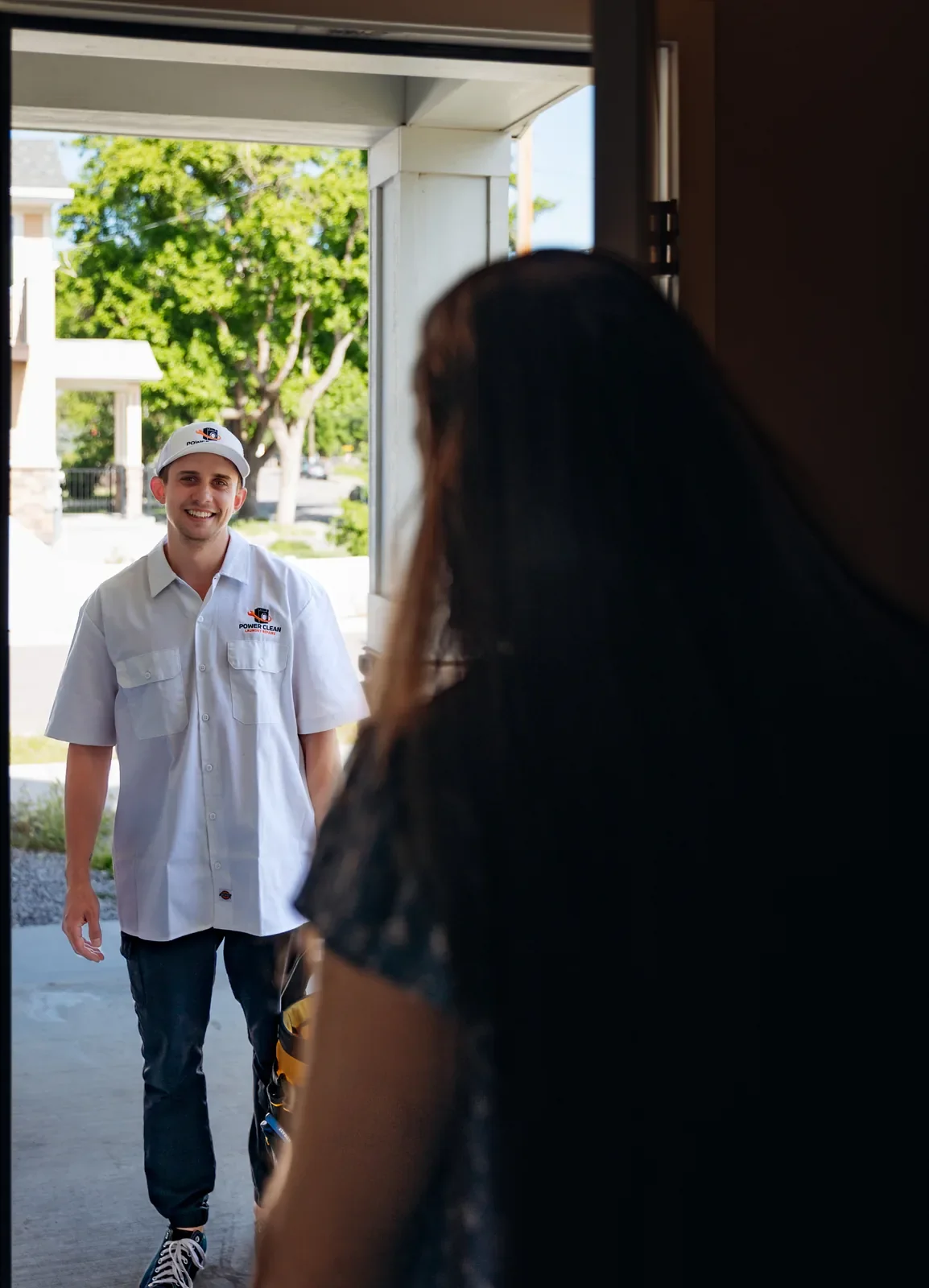 Blake from PowerClean smiling as he walks up to an open front door with his tool bag, seen from inside past a homeowner