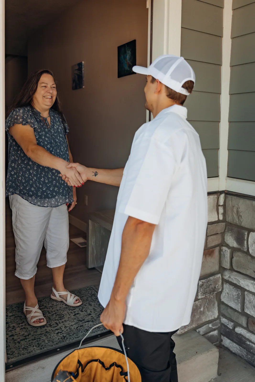 Blake from PowerClean, tool bag in hand, shaking hands with a smiling homeowner standing in her front doorway