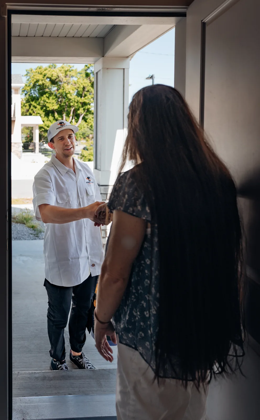 A homeowner at her open front door shaking hands with Blake from PowerClean, seen from inside the home
