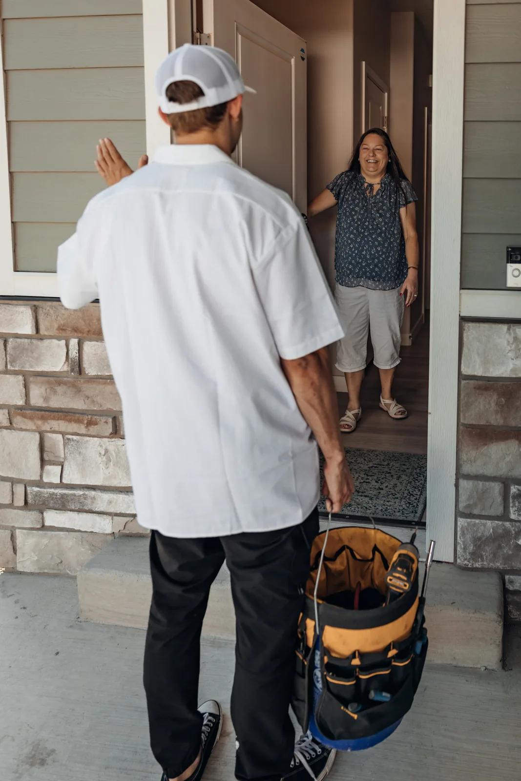 Blake from PowerClean carrying a tool bag and waving to a smiling homeowner standing in her front doorway