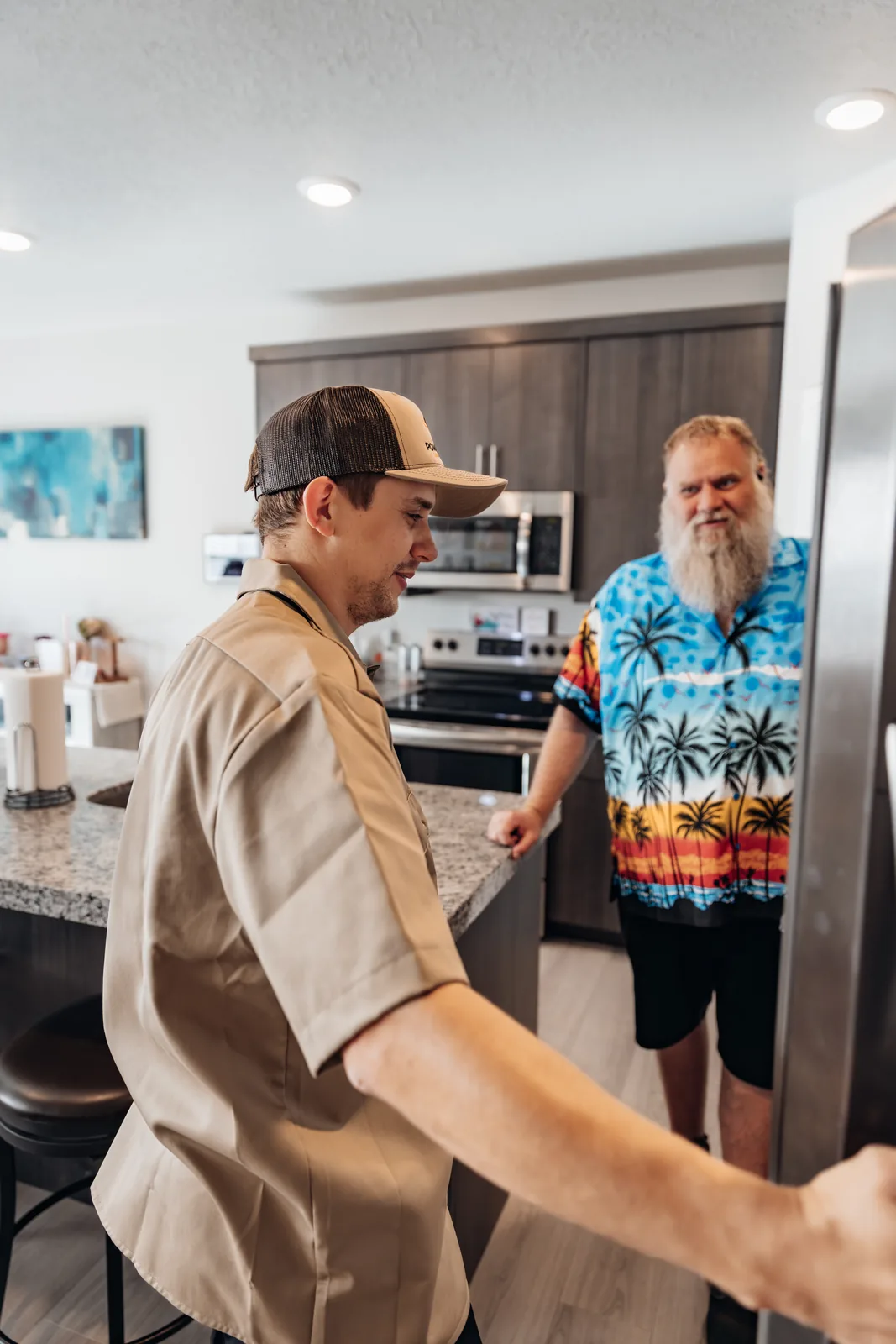 Blake from PowerClean smiling, one hand on a stainless steel refrigerator door, as a customer facing him rests a hand on the kitchen island