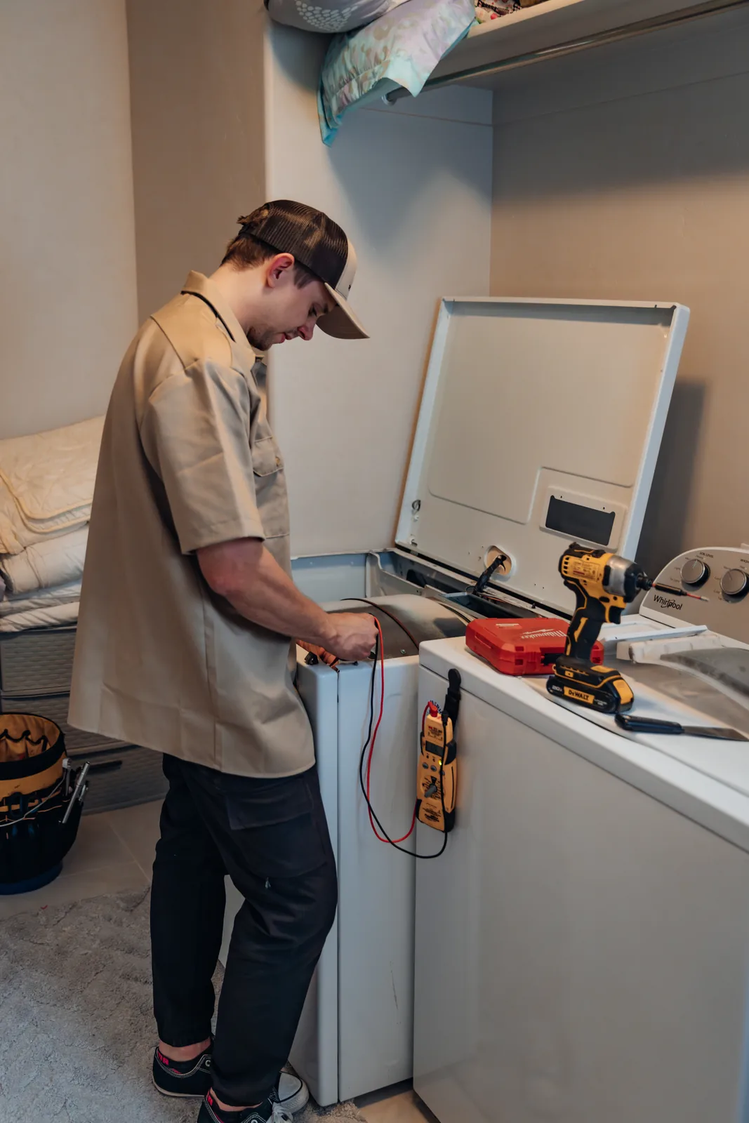 Blake from PowerClean holding multimeter leads at a dryer with its top panel raised, the meter hanging from the washer beside it