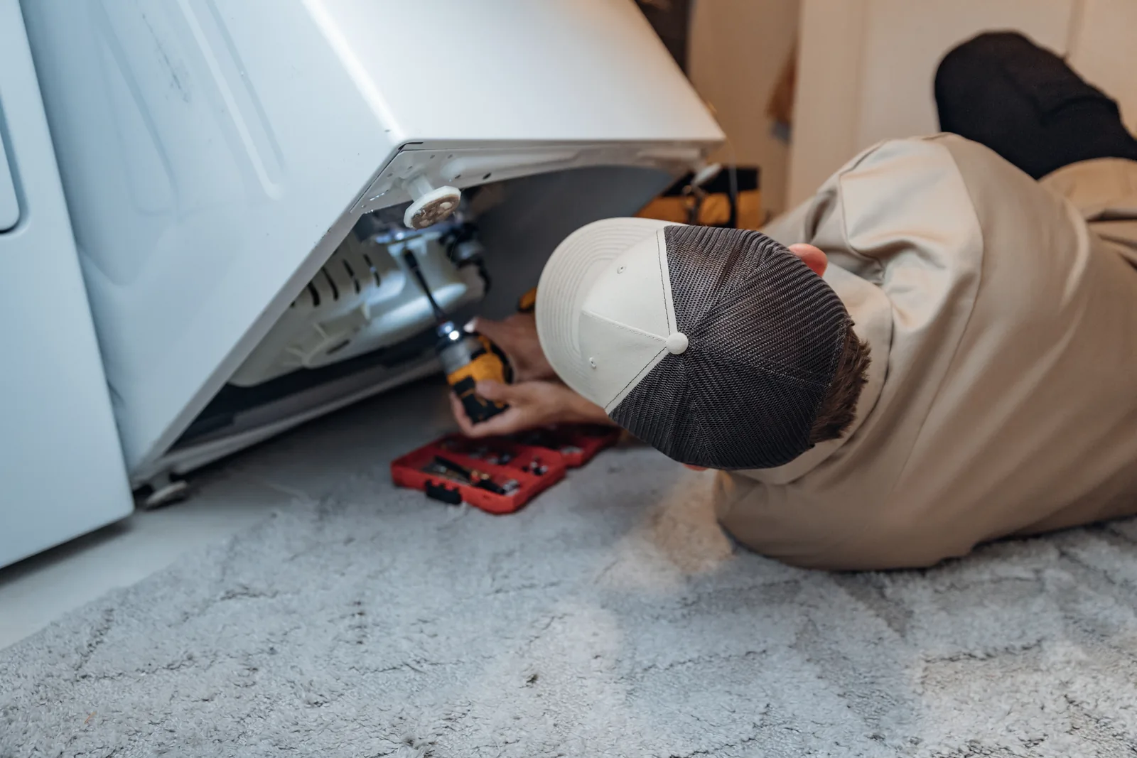 Close-up of Blake from PowerClean working on the underside of a tilted-up washer, his bit case open on the floor